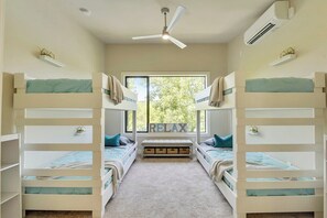 Une chambre avec des lits superposés, un ventilateur de plafond, un appareil de climatisation et une fenêtre donnant sur des arbres.