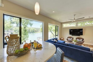 A modern living room with a large window, a flat-screen TV, and a blue sofa. - Minutes to Downtown Austin: Peaceful Waterfront Retreat with City Access Nearby (Austin)