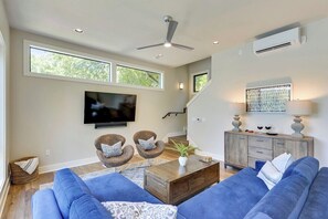 A modern living room with a flat-screen TV, two armchairs, a sofa, a coffee table, and a staircase leading to an upper level.