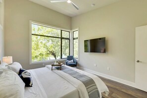 A bedroom with a bed, a chair, a TV, and a window with a view of trees.