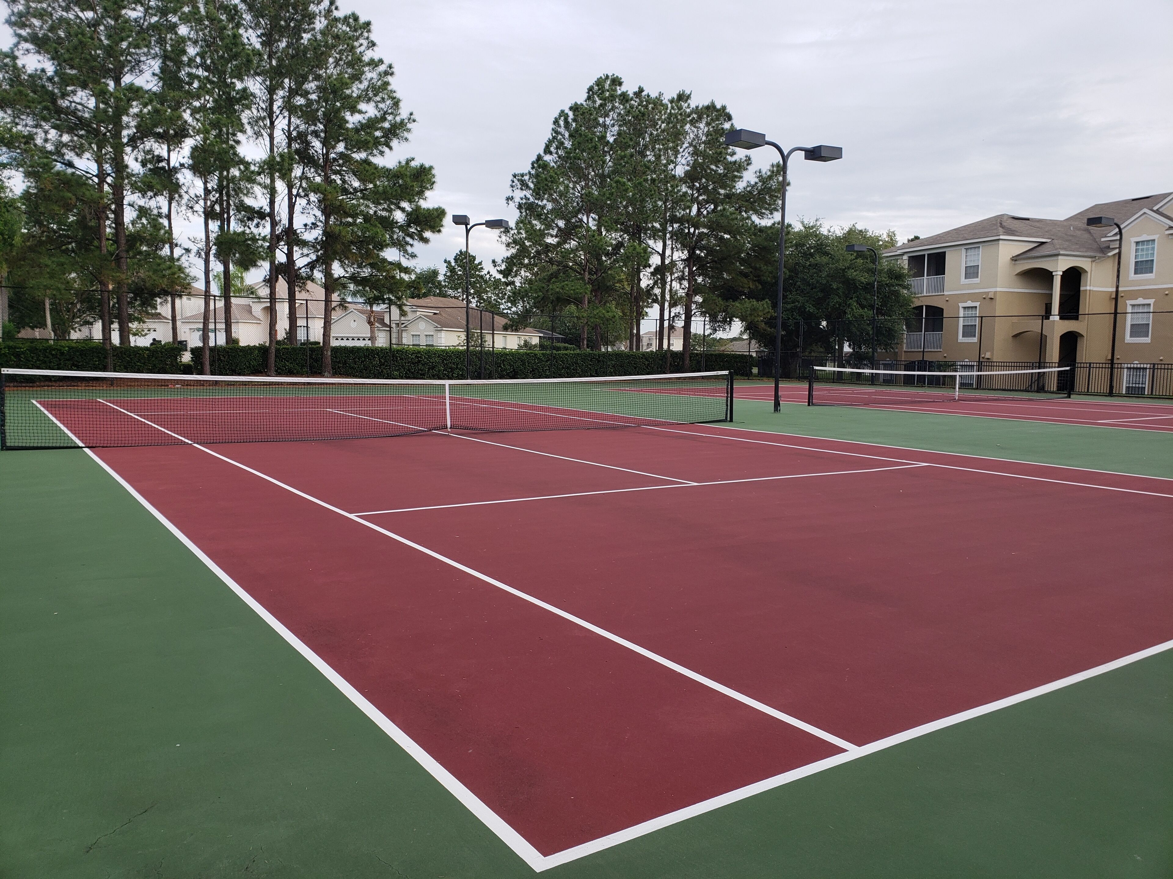 Un court de tennis avec un filet, entouré d’arbres et de bâtiments.