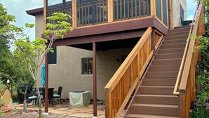 A two-story house with a wooden deck, a staircase, and a patio area with outdoor furniture.
