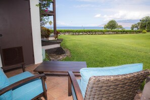 Une terrasse avec vue sur l’océan, une pelouse et un bâtiment doté d’une porte et d’une fenêtre.