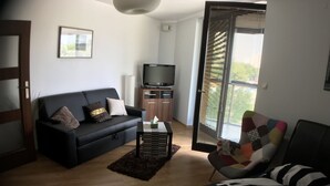 Ein modernes Wohnzimmer mit einer schwarzen Couch, einem Fernseher und einem farbenfrohen Sessel.
