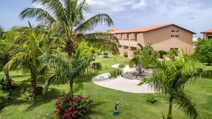 Un patio de hotel con palmeras, un jardín circular central y un edificio de techo rojo.