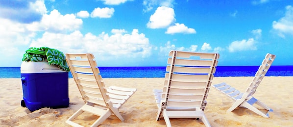 Strandstühle und eine Kühlbox an einem sandigen Strand unter blauem Himmel.