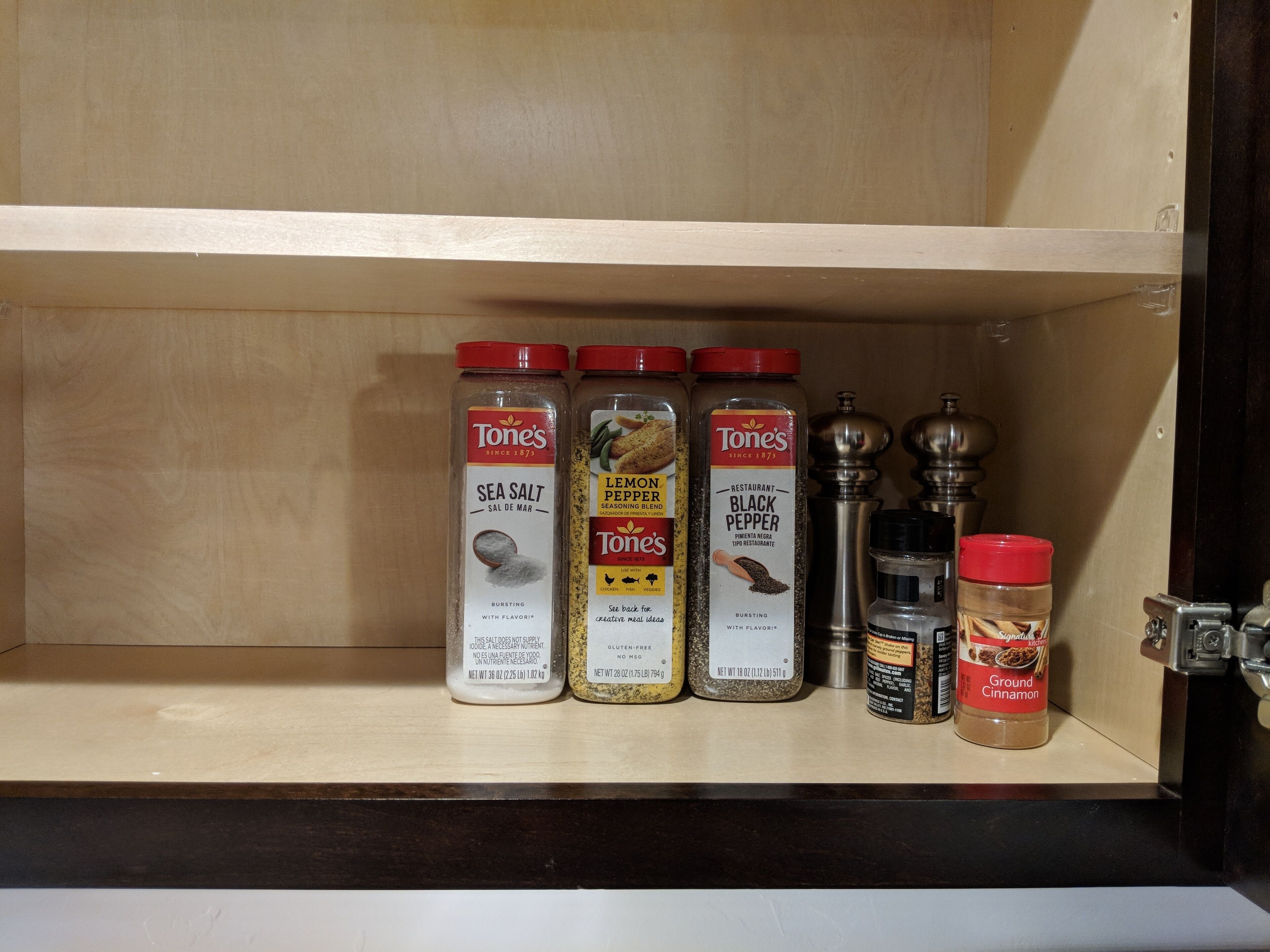 A kitchen shelf with four spice containers and a pepper grinder.
