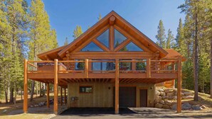 A log cabin with a balcony, a garage, and a stone foundation.