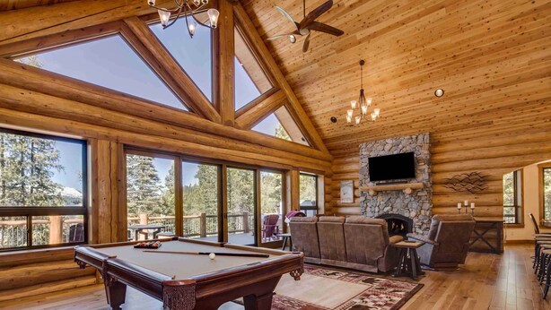 A spacious lodge with a pool table, comfortable seating, a stone fireplace, and large windows offering mountain views.