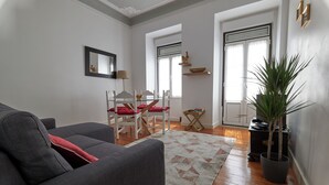 Ein Wohnzimmer mit einer Couch, einem Esstisch mit Stühlen, einer Topfpflanze und einem Teppich.