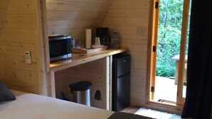 Una habitación de cabaña acogedora con una cama, una kitchenette con microondas, cafetera y refrigerador.