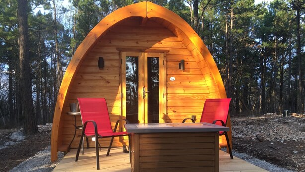 Una cabaña de madera con techo curvo, dos sillas rojas y una mesa en frente.