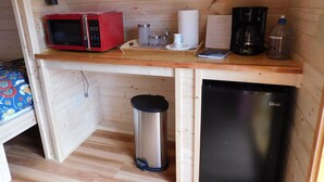 Una kitchenette compacta con un microondas rojo, cafetera y lavavajillas negro.