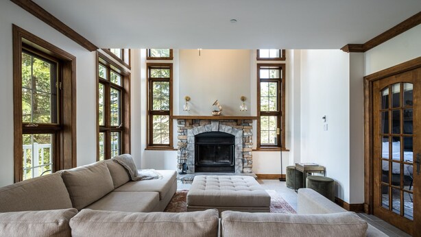 A spacious living room with a stone fireplace, large windows, and a sectional sofa.