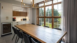 A modern kitchen with a wooden dining table, black chairs, and a large window with a view of trees.