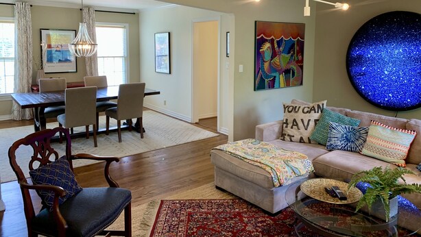 A living room with a dining area, a round wall art piece, and a sofa with decorative pillows.