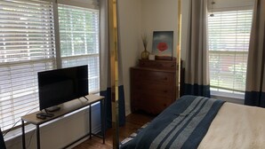 A bedroom with a bed, a TV on a stand, a dresser, and a window with blinds.