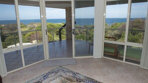 A spacious room with large glass doors leading to a balcony with a view of the sea. - Oceana Sunset - Beachfront family friendly home with amazing ocean views (Warnbro)