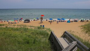 Ein Strand mit einer Holzpromenade, die zum Ufer führt, mit einem Rettungsturm und mehreren Strandsonnenschirmen.