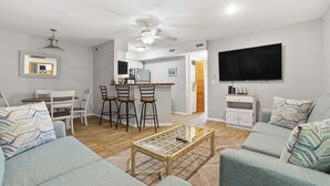Ein modernes Wohnzimmer mit einer Couch, einem Couchtisch, einem Fernseher und einer Küchenzeile mit Bar.