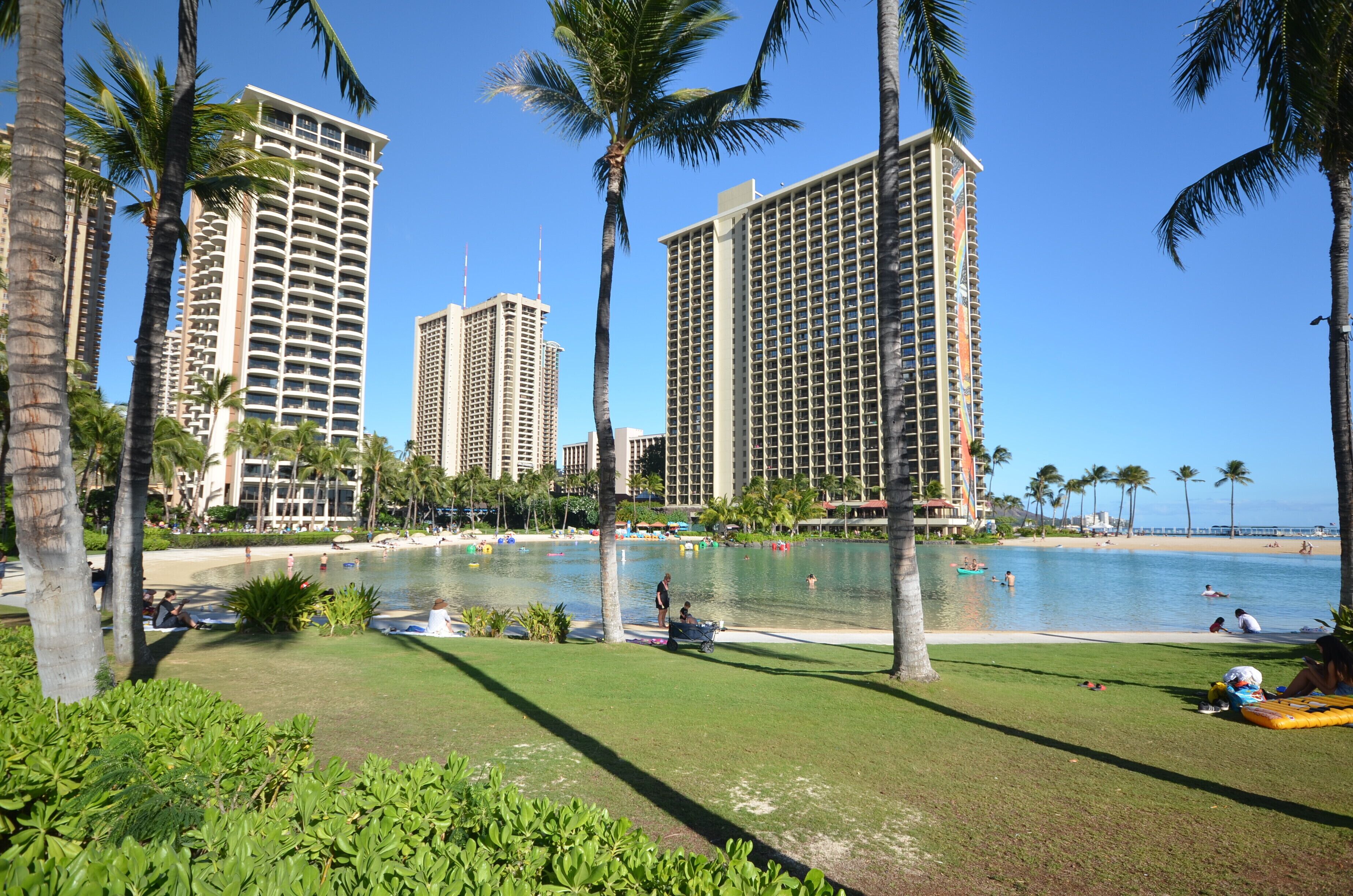 A beachfront resort with high-rise buildings, a pool area, and palm trees.