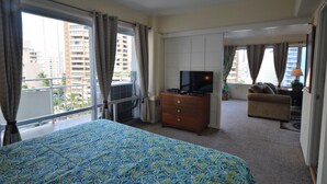 Ett hotellrum med en stor säng, en TV, en byrå och en balkong med gardiner.