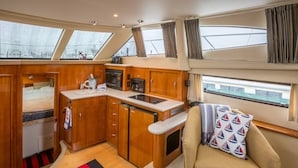 A compact galley with wooden cabinetry, a microwave, and a sink. There is a small bed with a red and black striped rug. - Boston Harbor Yacht,  AC/Heat, Walk to North End WiFi (Boston)