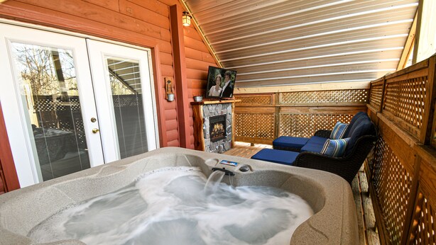 Ein Whirlpool mit Steinverkleidung, ein Kamin und eine Holzterrasse mit Überdachung.