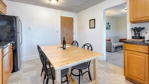 A compact kitchen with a wooden table, black chairs, a refrigerator, and wooden cabinets.