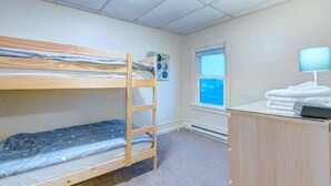 A dormitory room with bunk beds, a desk with a lamp, a window, and a radiator.