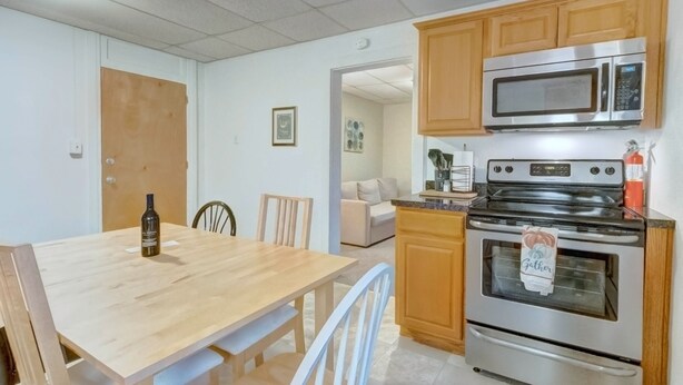 A kitchen with wooden cabinets, a stainless steel oven, a microwave, and a dining table with chairs.