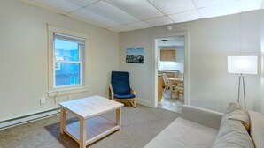 A room with a wooden table, a blue chair, a beige sofa, a window, and a door leading to a kitchen.