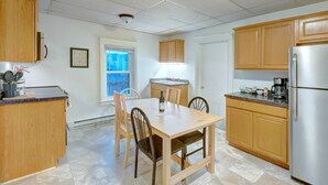 A kitchen with wooden cabinets, a stainless steel refrigerator, a dining table with chairs, and a window with a view of buildings.