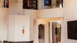 Un intérieur spacieux avec une cheminée, un escalier menant à un balcon et une vue sur l’extérieur.
