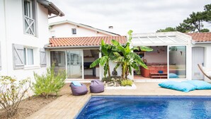 Une maison moderne dotée d’une piscine, d’un patio avec des sièges et d’un jardin.