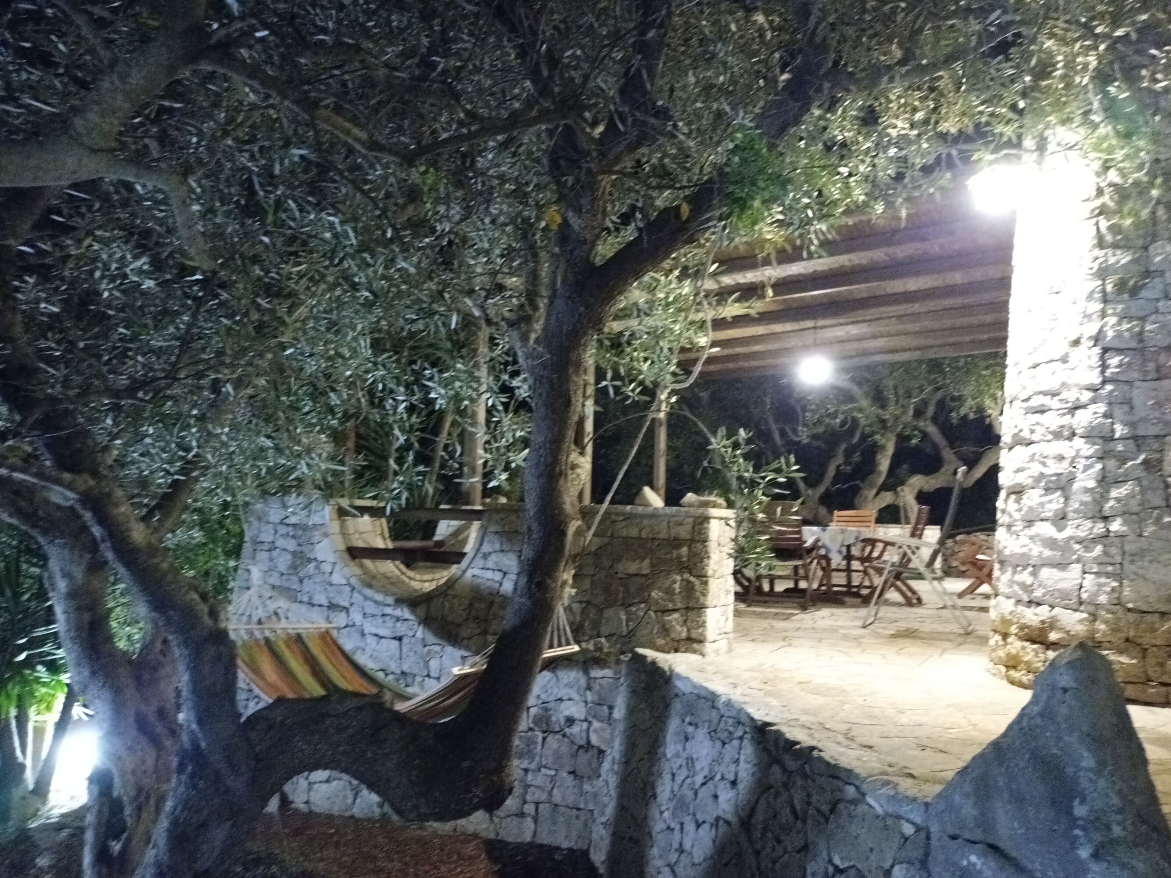 An outdoor patio area with stone walls, a hammock, and a pergola with lights.