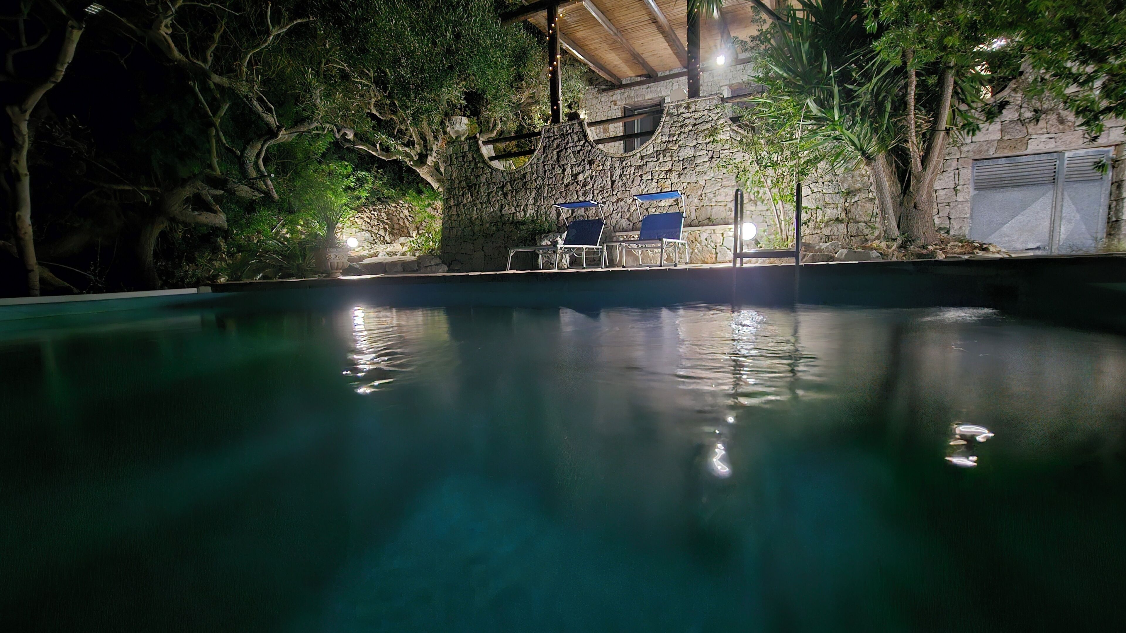 A swimming pool with a stone wall and trees in the background.