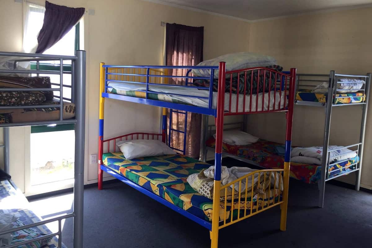 A dormitory room with bunk beds, a window with curtains, and a ceiling fan.