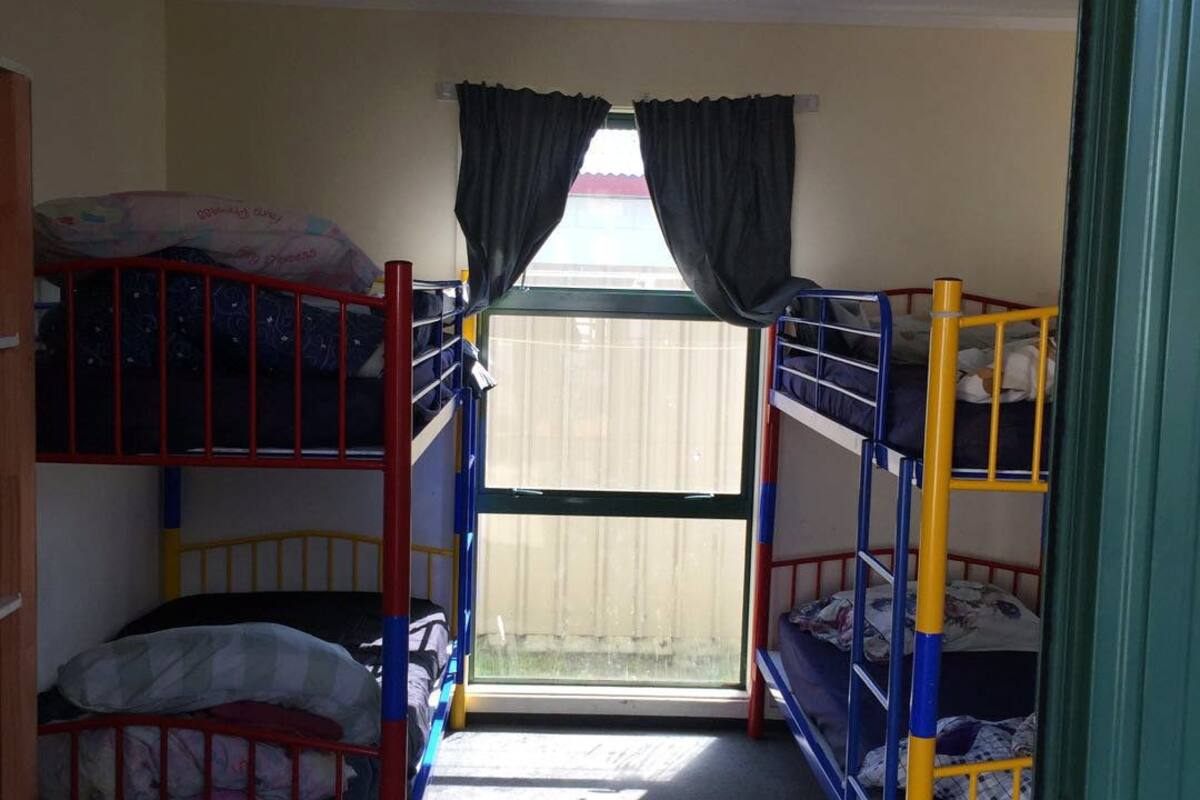 A dormitory room with bunk beds, a window with curtains, and a ceiling fan.