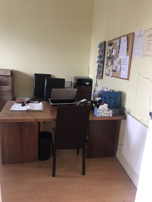 Un petit bureau avec un bureau, deux ordinateurs, une chaise et un tableau d’affichage où sont accrochés des documents.