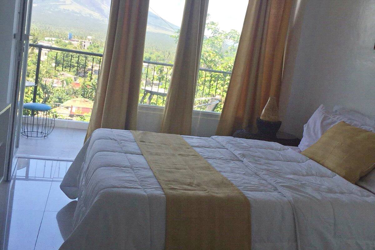 A hotel room with a large bed, a balcony with a view of a mountain, and curtains.