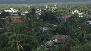 A mountain with a cloud-covered peak, a town with buildings and greenery in the foreground.