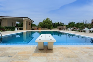 Piscina con una mesa en el centro, rodeada de sillones de descanso y una zona de estar cubierta.