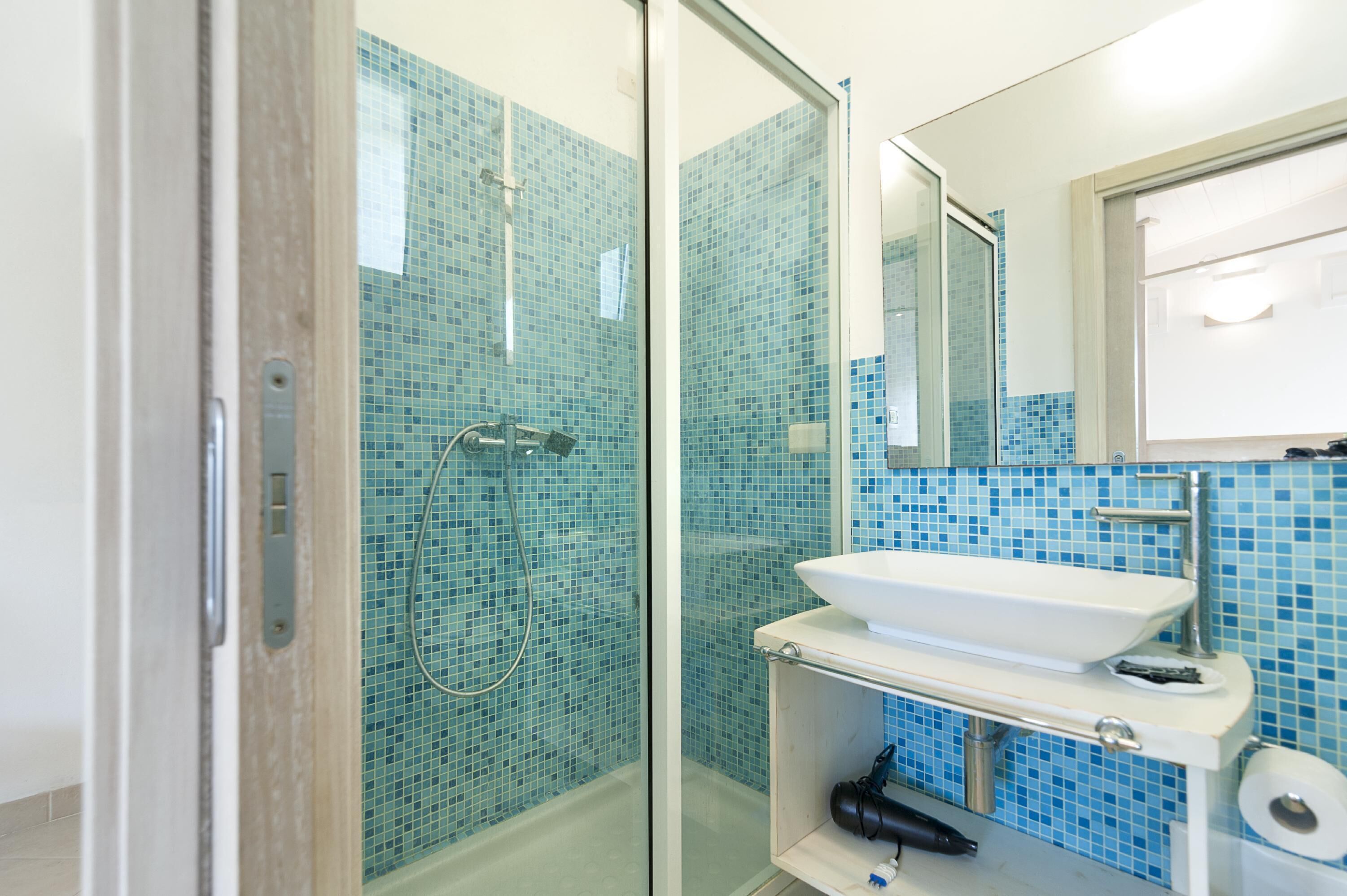 A modern bathroom with a glass shower enclosure, a white sink, and a blue-tiled wall.
