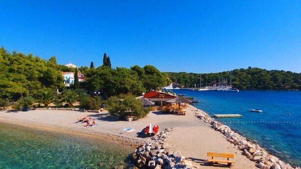 Eine Küstenlandschaft mit Sandstrand, einem kleinen Gebäude mit rotem Dach und klarem, blauem Wasser.