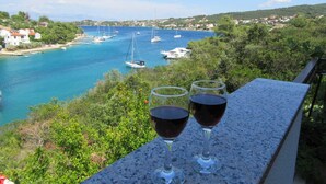Ein malerischer Blick auf eine Küstenstadt mit Booten auf dem Wasser und zwei Gläsern Rotwein auf einem Balkon.
