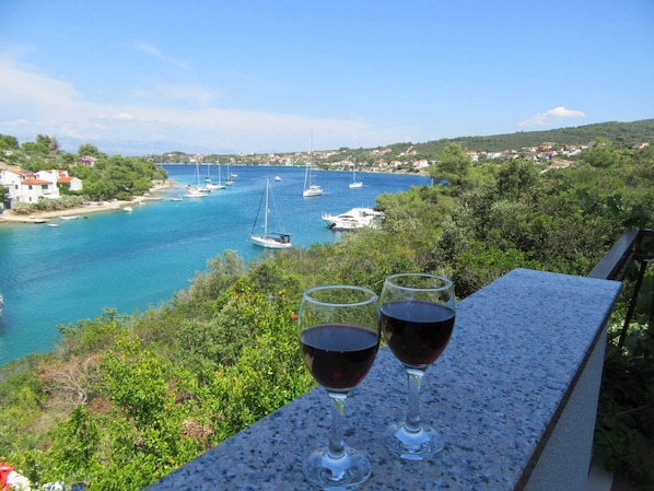 A scenic view of a coastal town with boats on the water and two glasses of red wine on a balcony.