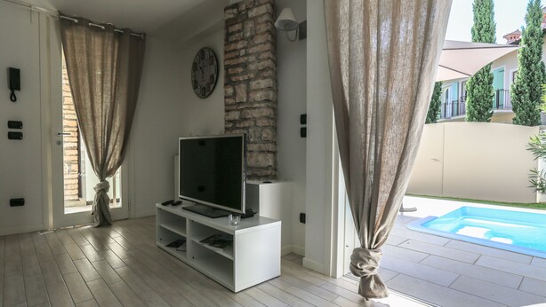 A living room with a TV on a white stand, a stone wall, and a view of a swimming pool.