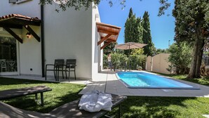 A poolside area with a lounge chair, a bench, and a covered seating area.