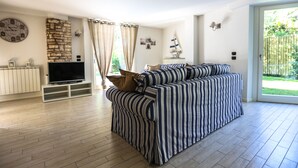 A modern living room with a striped sofa, a flat-screen TV, a stone wall, and a large window with curtains.